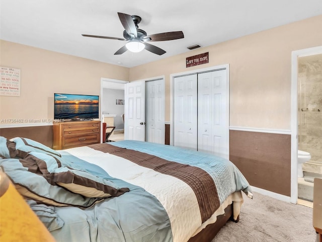 bedroom with multiple closets, ensuite bath, carpet flooring, and ceiling fan