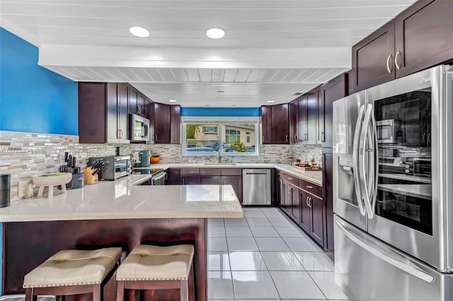 kitchen featuring sink, a breakfast bar area, backsplash, kitchen peninsula, and stainless steel appliances