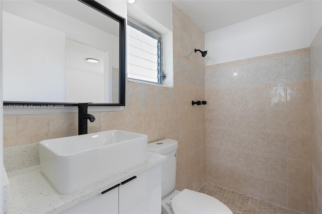 bathroom with vanity, toilet, tile walls, and a tile shower