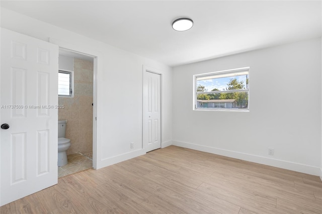 unfurnished bedroom featuring a closet, connected bathroom, multiple windows, and light wood-type flooring