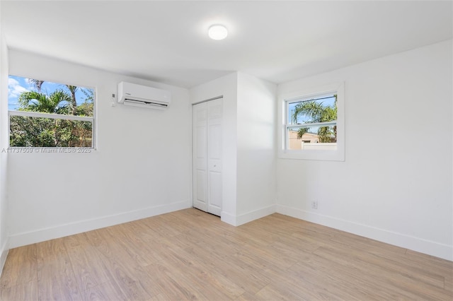 unfurnished bedroom featuring a wall unit AC, a closet, and light wood-type flooring