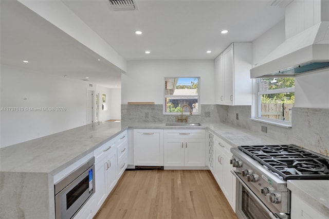 kitchen with sink, wall chimney range hood, kitchen peninsula, stainless steel appliances, and white cabinets