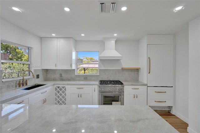 kitchen featuring premium range hood, high end stove, white cabinetry, sink, and light stone counters