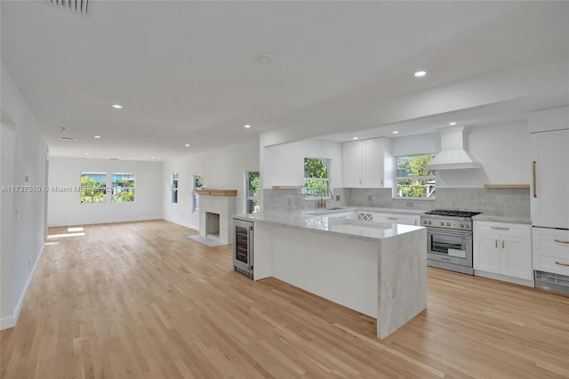 kitchen with high end stainless steel range oven, white cabinetry, light stone countertops, custom exhaust hood, and kitchen peninsula