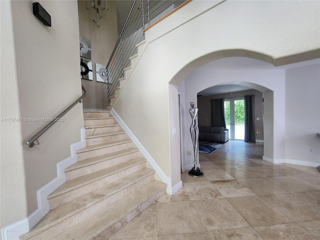 staircase featuring arched walkways, a towering ceiling, and baseboards