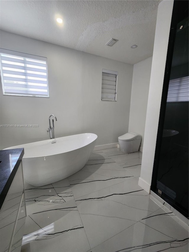 bathroom with baseboards, visible vents, marble finish floor, a textured ceiling, and a freestanding tub