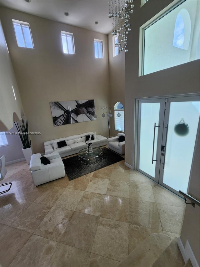 living room with french doors, a healthy amount of sunlight, a towering ceiling, and baseboards