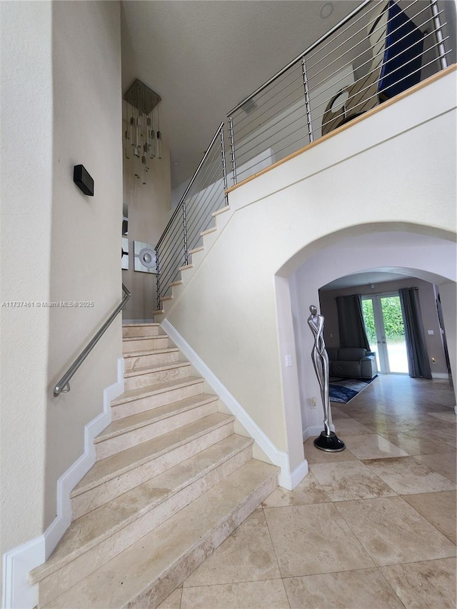 staircase featuring baseboards, a high ceiling, arched walkways, and french doors