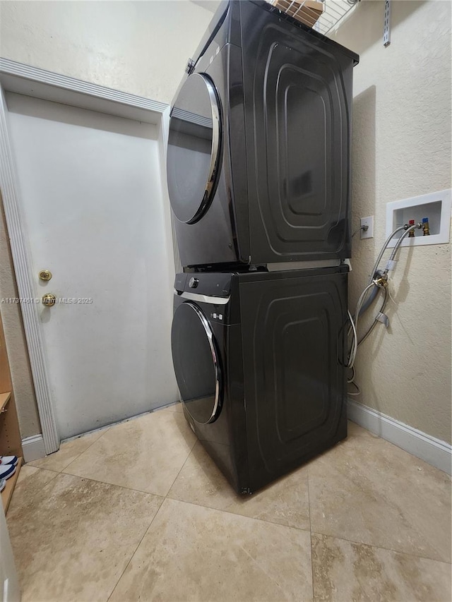 laundry room featuring laundry area, baseboards, stacked washer / dryer, and light tile patterned flooring