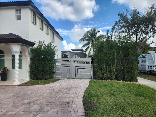 view of side of home featuring a tile roof, a gate, a lawn, and stucco siding