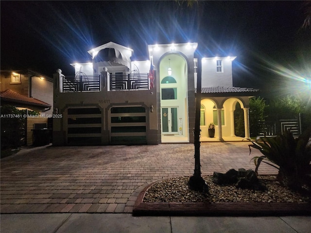 view of front facade featuring a balcony, stucco siding, decorative driveway, and french doors