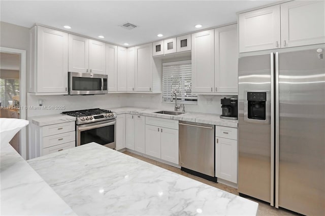 kitchen featuring stainless steel appliances, light stone countertops, sink, and white cabinets