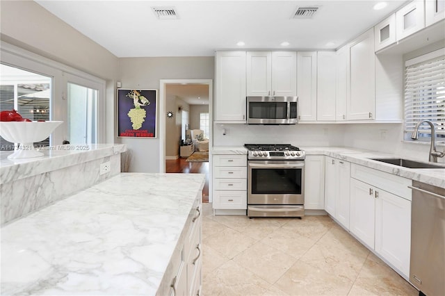 kitchen featuring sink, appliances with stainless steel finishes, a wealth of natural light, light stone countertops, and white cabinets