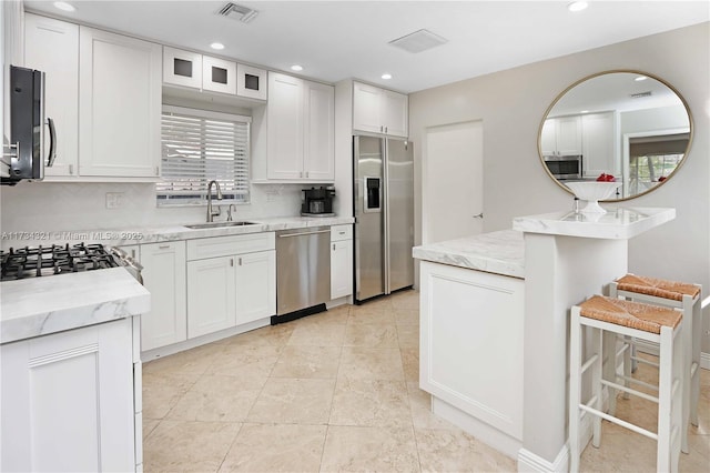 kitchen with sink, white cabinetry, appliances with stainless steel finishes, a kitchen breakfast bar, and backsplash