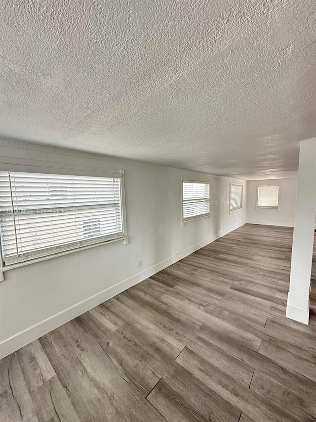 empty room featuring a textured ceiling, baseboards, and wood finished floors