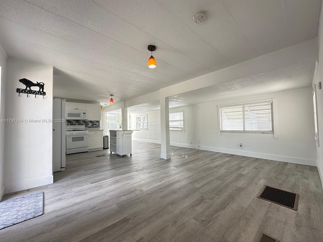 unfurnished living room with visible vents, light wood-style flooring, a textured ceiling, and baseboards