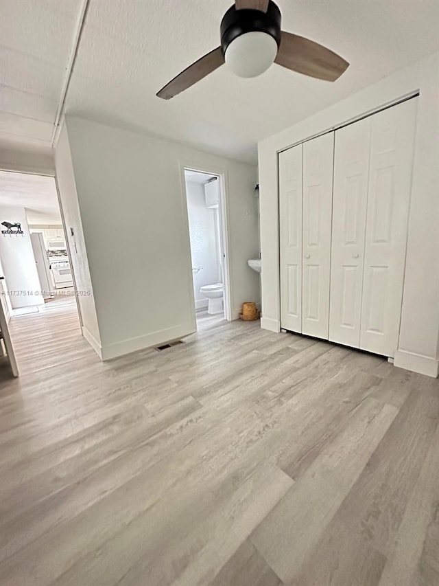 unfurnished bedroom with wood finished floors, visible vents, baseboards, a closet, and connected bathroom