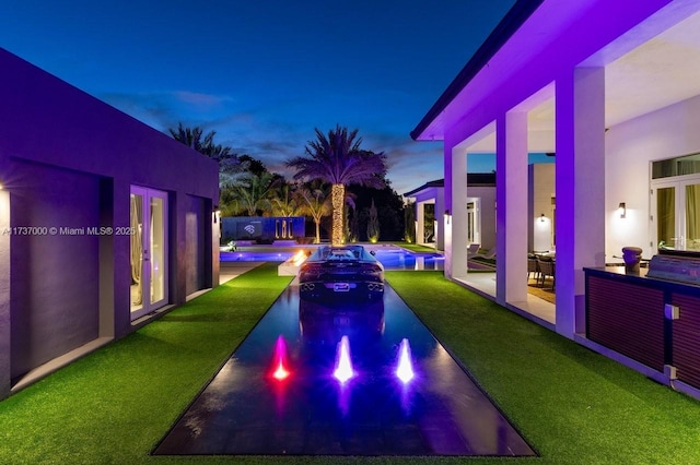 pool at dusk featuring a patio, a yard, and french doors