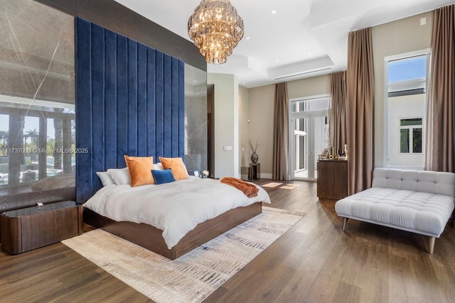 bedroom with hardwood / wood-style flooring, a tray ceiling, a chandelier, and access to outside