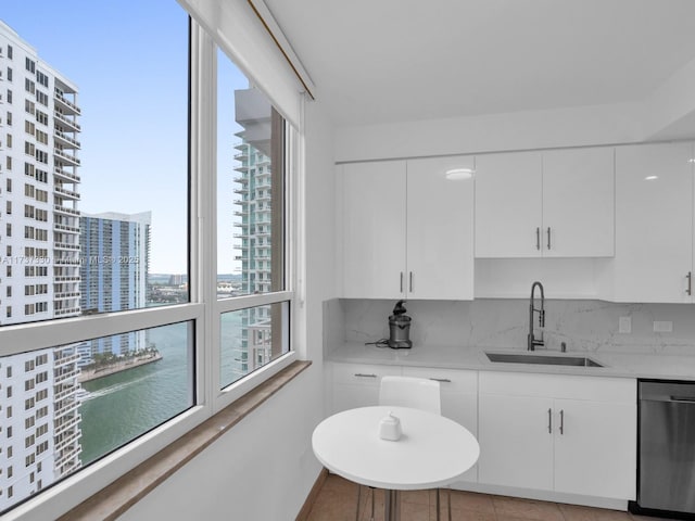 kitchen featuring sink, dishwasher, white cabinetry, a water view, and light stone countertops