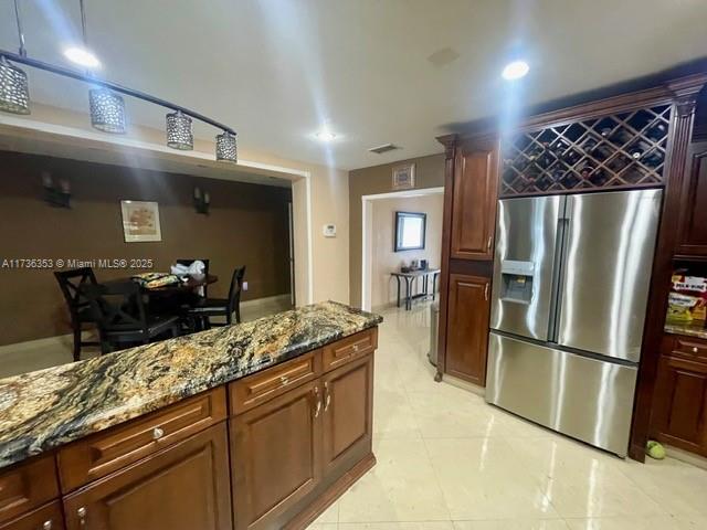 kitchen featuring stone counters, light tile patterned flooring, stainless steel fridge, and visible vents