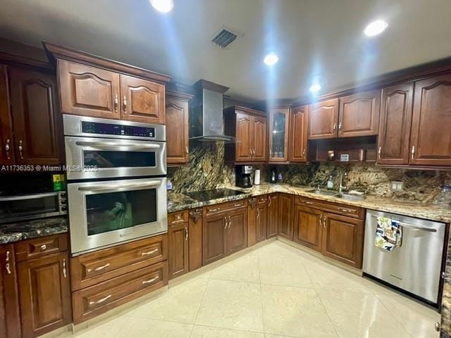 kitchen with stainless steel appliances, wall chimney range hood, stone countertops, and a sink