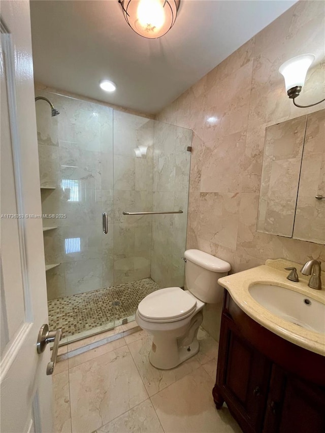 bathroom with toilet, vanity, tile walls, marble finish floor, and a stall shower