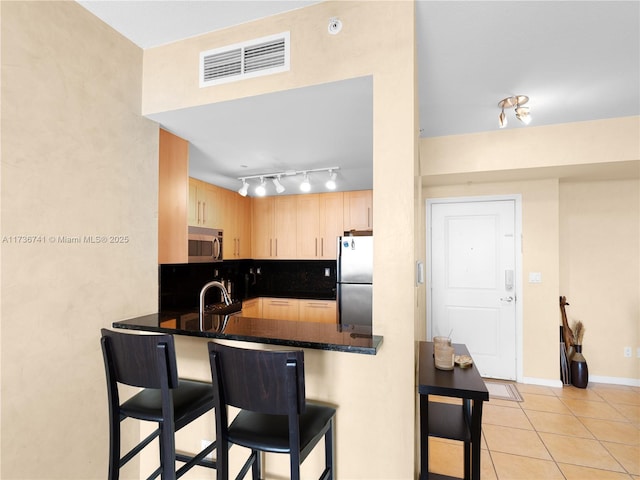 kitchen with light brown cabinetry, dark stone counters, light tile patterned floors, kitchen peninsula, and stainless steel appliances