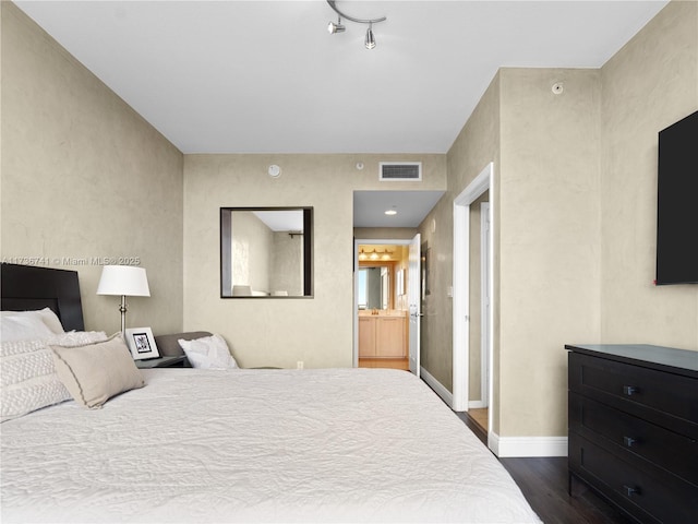 bedroom with dark wood-type flooring and connected bathroom