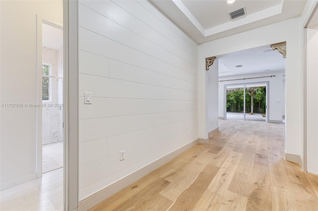 corridor with light hardwood / wood-style floors and a tray ceiling