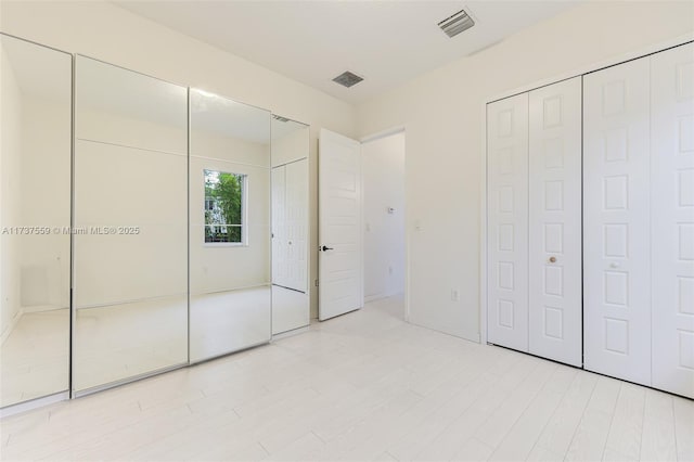 unfurnished bedroom featuring multiple closets and light hardwood / wood-style flooring