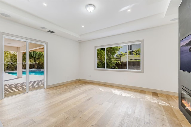 unfurnished room with a tray ceiling, light hardwood / wood-style floors, and a wealth of natural light