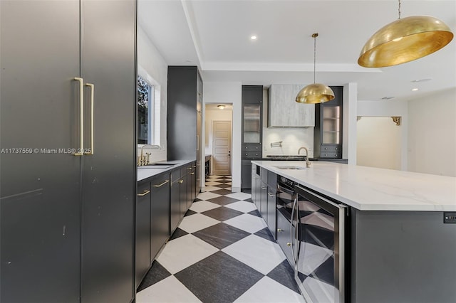 kitchen with an island with sink, sink, wine cooler, and decorative light fixtures