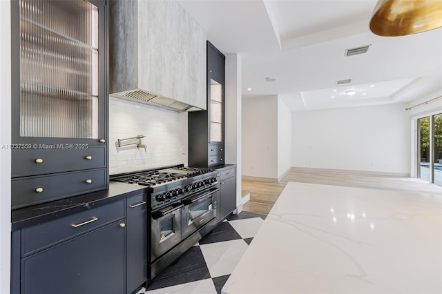 kitchen with tasteful backsplash, dark hardwood / wood-style floors, a tray ceiling, dark stone counters, and range with two ovens