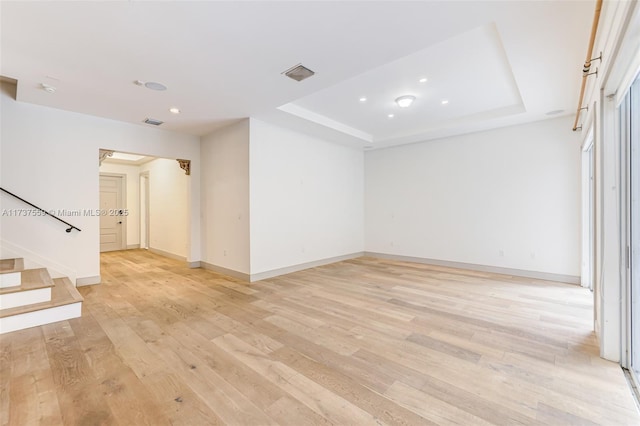 empty room featuring a tray ceiling and light hardwood / wood-style floors