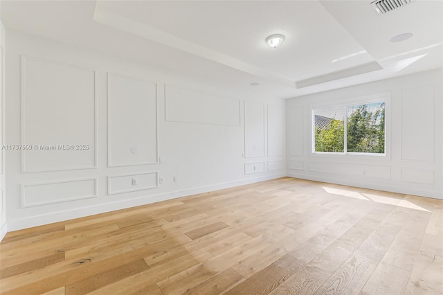 unfurnished room with a tray ceiling and light wood-type flooring