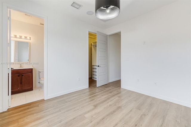 unfurnished bedroom featuring ensuite bath, a spacious closet, a closet, and light wood-type flooring