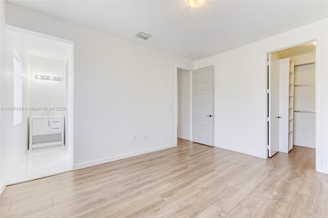 unfurnished bedroom with a walk in closet, light hardwood / wood-style flooring, and ensuite bathroom