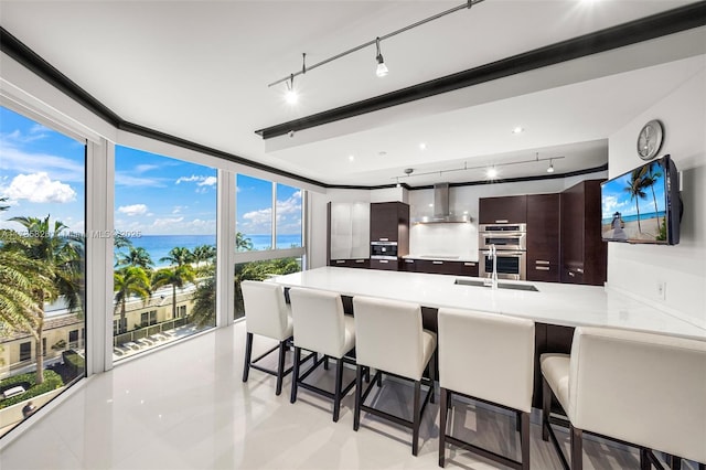 kitchen with wall chimney exhaust hood, a breakfast bar, kitchen peninsula, and dark brown cabinets