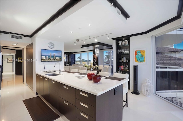 kitchen featuring a breakfast bar, an island with sink, sink, crown molding, and dark brown cabinets