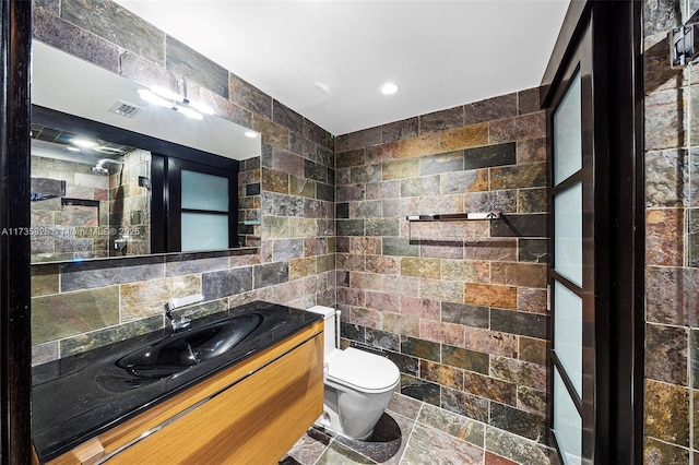 bathroom featuring vanity, toilet, and tile walls