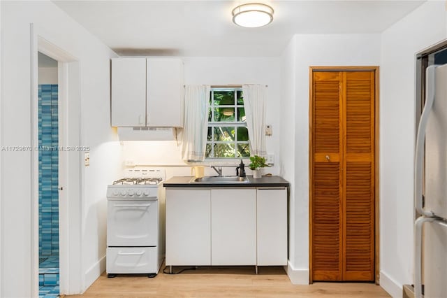 2424 Prairie Ave, Miami Beach, FL 33140 - kitchen with white range with gas cooktop, a sink, freestanding refrigerator, dark countertops, and under cabinet range hood