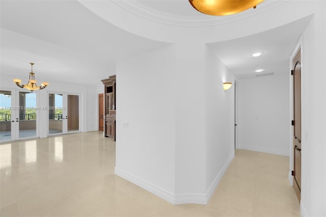 corridor featuring french doors, ornamental molding, and an inviting chandelier