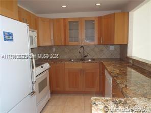 kitchen with sink, white appliances, tasteful backsplash, light stone counters, and kitchen peninsula