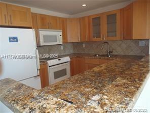 kitchen with sink, white appliances, light stone counters, decorative backsplash, and kitchen peninsula