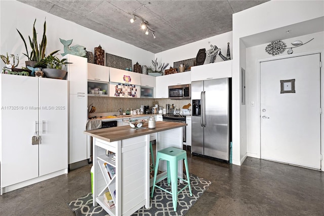 kitchen with butcher block countertops, a breakfast bar area, stainless steel appliances, tasteful backsplash, and white cabinets