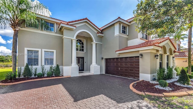 mediterranean / spanish home featuring decorative driveway, an attached garage, a tile roof, and stucco siding