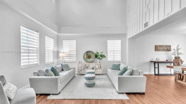 living area featuring a towering ceiling, baseboards, and wood finished floors