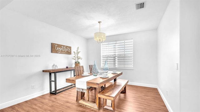 dining space featuring an inviting chandelier, baseboards, visible vents, and wood finished floors