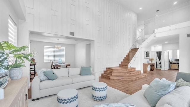 living area with a chandelier, a high ceiling, wood finished floors, visible vents, and stairs